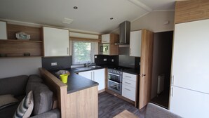 A compact kitchen with a microwave, stove, and oven, a small dining area with a table and chairs, and a sofa with cushions. - Le Cabri Resort (Duras)