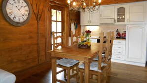 A wooden interior with a dining table, chairs, a chandelier, and a clock on the wall. - Cottage and Chalet Pr Klemuc (Bled)