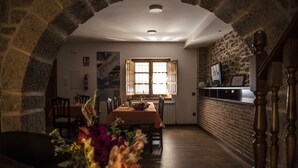 Zona de menjador acollidora amb taula preparada per a dues persones, arc de pedra i cuina amb pared de rajola i taulell de fusta.