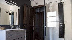 Un bany modern amb una cabina de dutxa de vidre, una porta de fusta i un lavabo amb mirall.