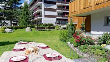 A hotel with a dining area set up outdoors, featuring a stone table with plates, glasses, and a loaf of bread.