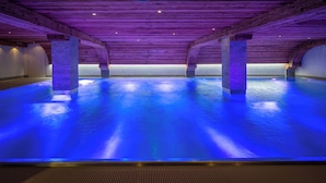 Una piscina interior con vigas de madera y suelo iluminado en azul.