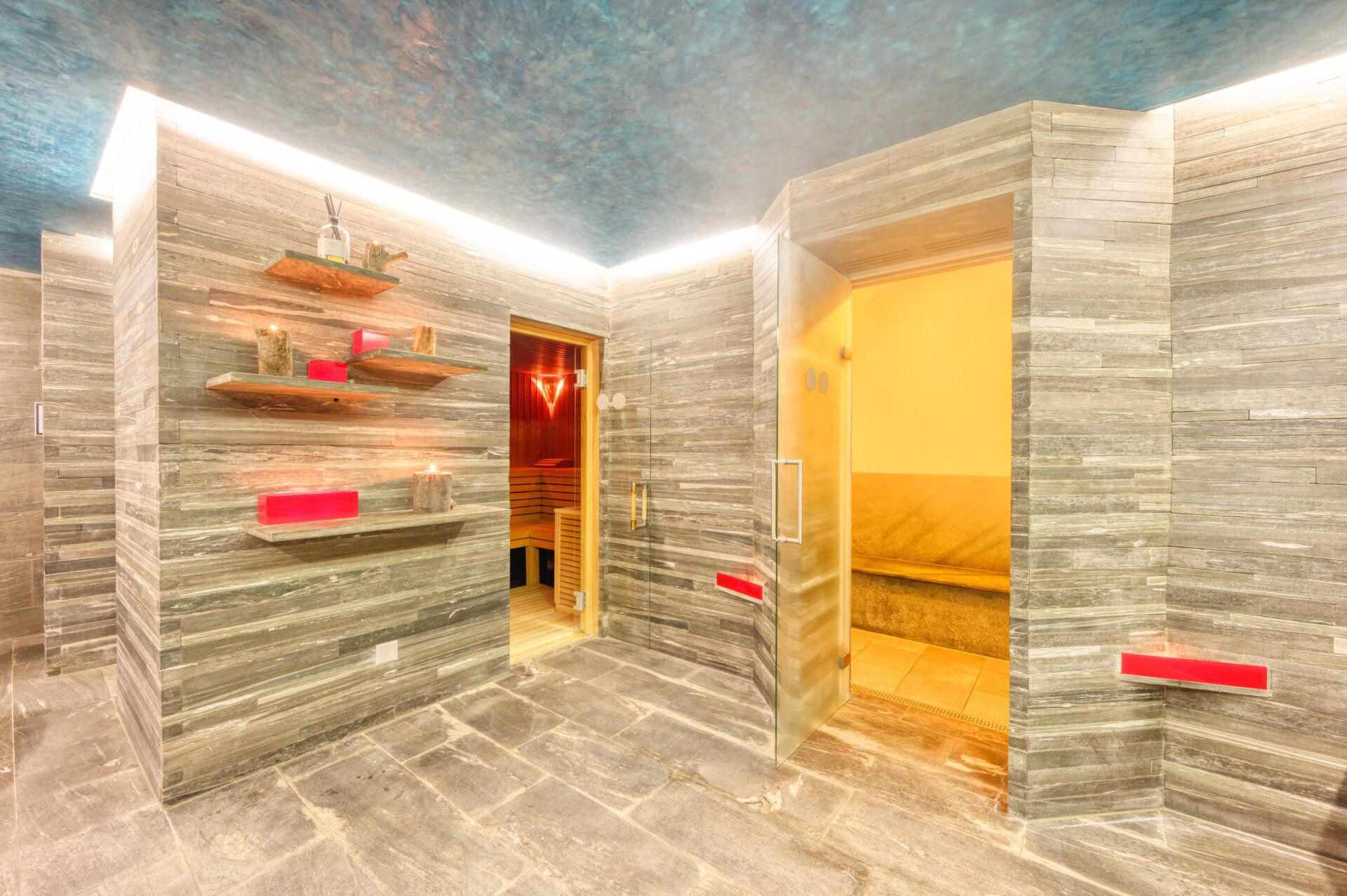 Une salle de spa moderne avec un mur en pierre, un banc en bois et une porte en verre donnant sur une autre pièce.