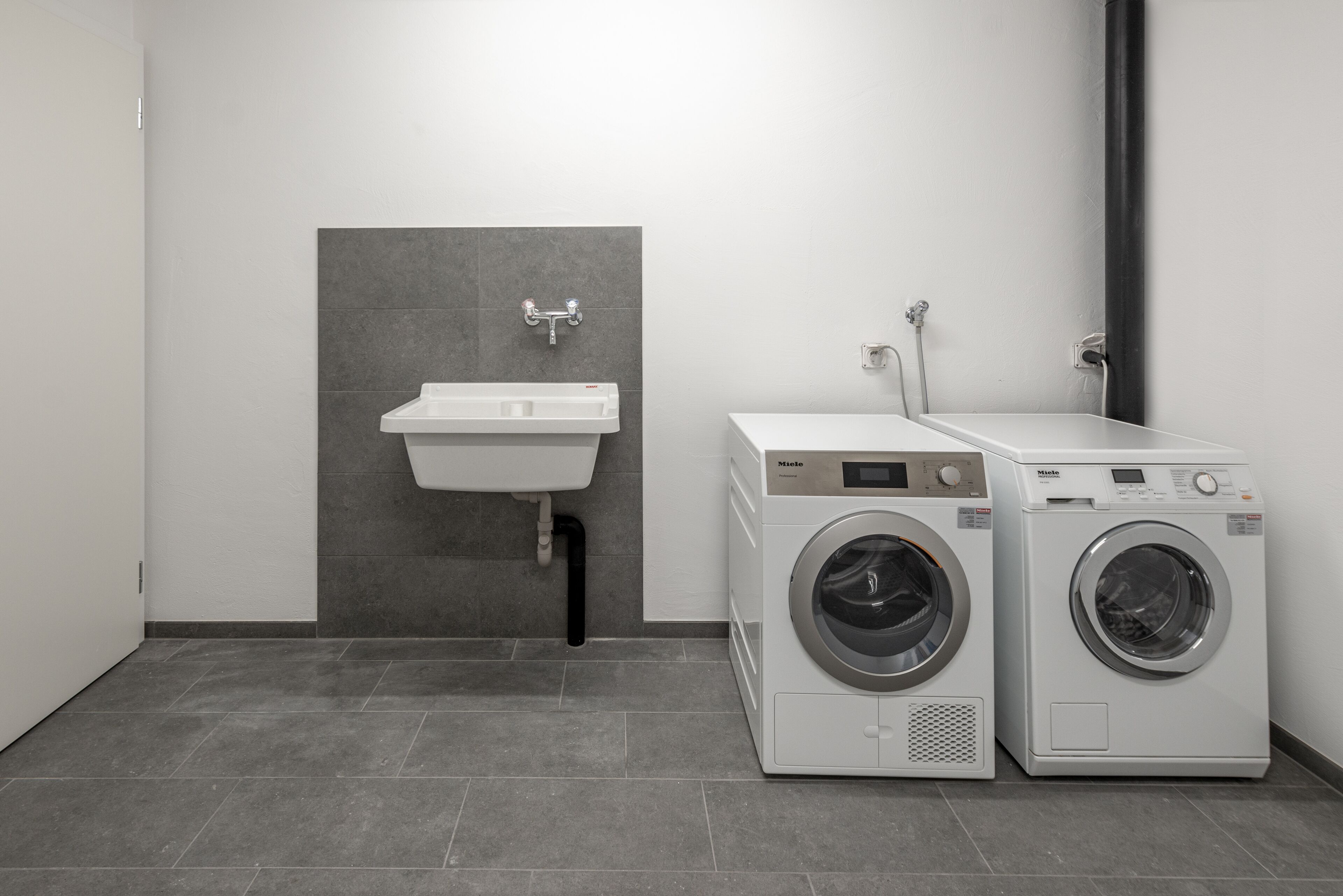 A laundry area with two front-loading washing machines and a wall-mounted sink.