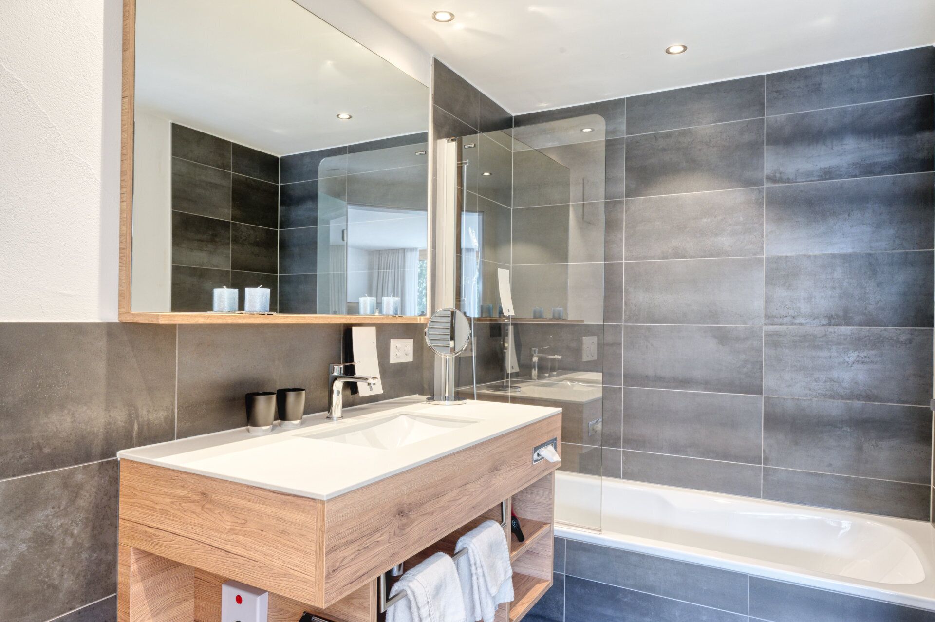 A modern bathroom with a wooden vanity, a large mirror, and a glass-enclosed shower area.
