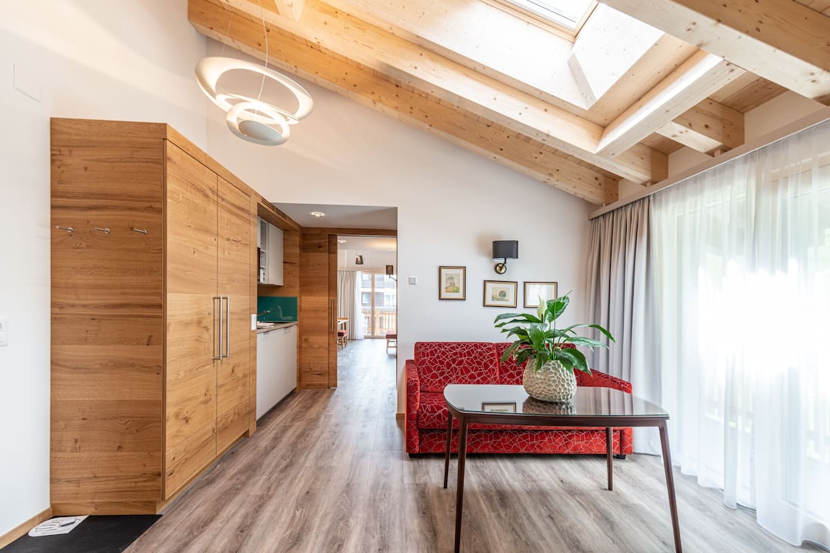 A modern living room with a red patterned sofa, a wooden dining table with a plant, and a skylight above.