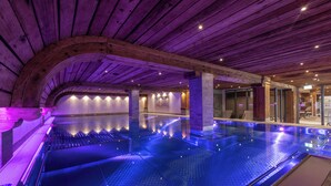 Una amplia piscina interior con techo y paredes de madera, rodeada de puertas y ventanas de vidrio.