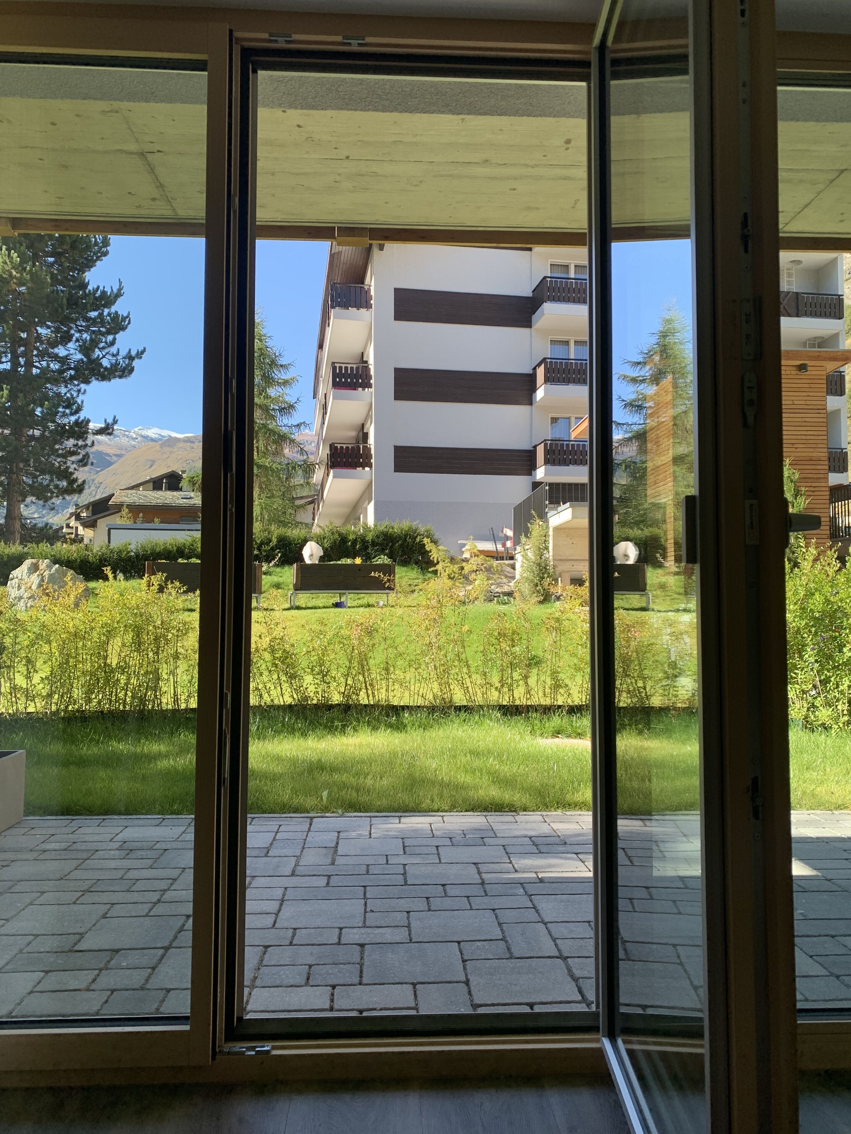 En modern byggnad med en entré av glas, en välskött gräsmatta och en bergig bakgrund.