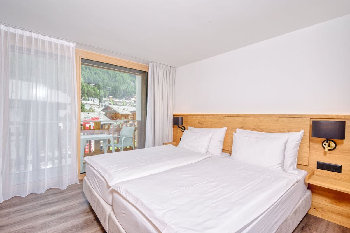 A hotel room with a large bed, wooden headboard, and a view of a village through a large window.