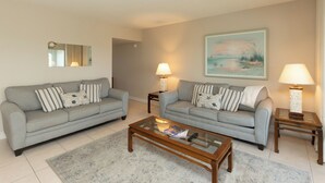A living room with two grey sofas, a glass coffee table, and two side tables with lamps. - San Marco Residence 604- Across the Street from Beach, Hotels, Restaurants and Shopping!  Sleeps 6! (Marco Island)