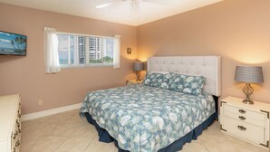 A bedroom with a large bed, two bedside tables, a ceiling fan, and a window with blinds. - San Marco Residence 604- Across the Street from Beach, Hotels, Restaurants and Shopping!  Sleeps 6! (Marco Island)