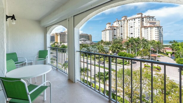 A balcony with a view of a beachfront hotel complex, including multiple high-rise buildings and palm trees. - San Marco Residence 604- Across the Street from Beach, Hotels, Restaurants and Shopping!  Sleeps 6! (Marco Island)