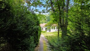 Un chemin mène à un bâtiment blanc surmonté d’un toit rouge, qui est entouré d’un feuillage verdoyant et dense.
