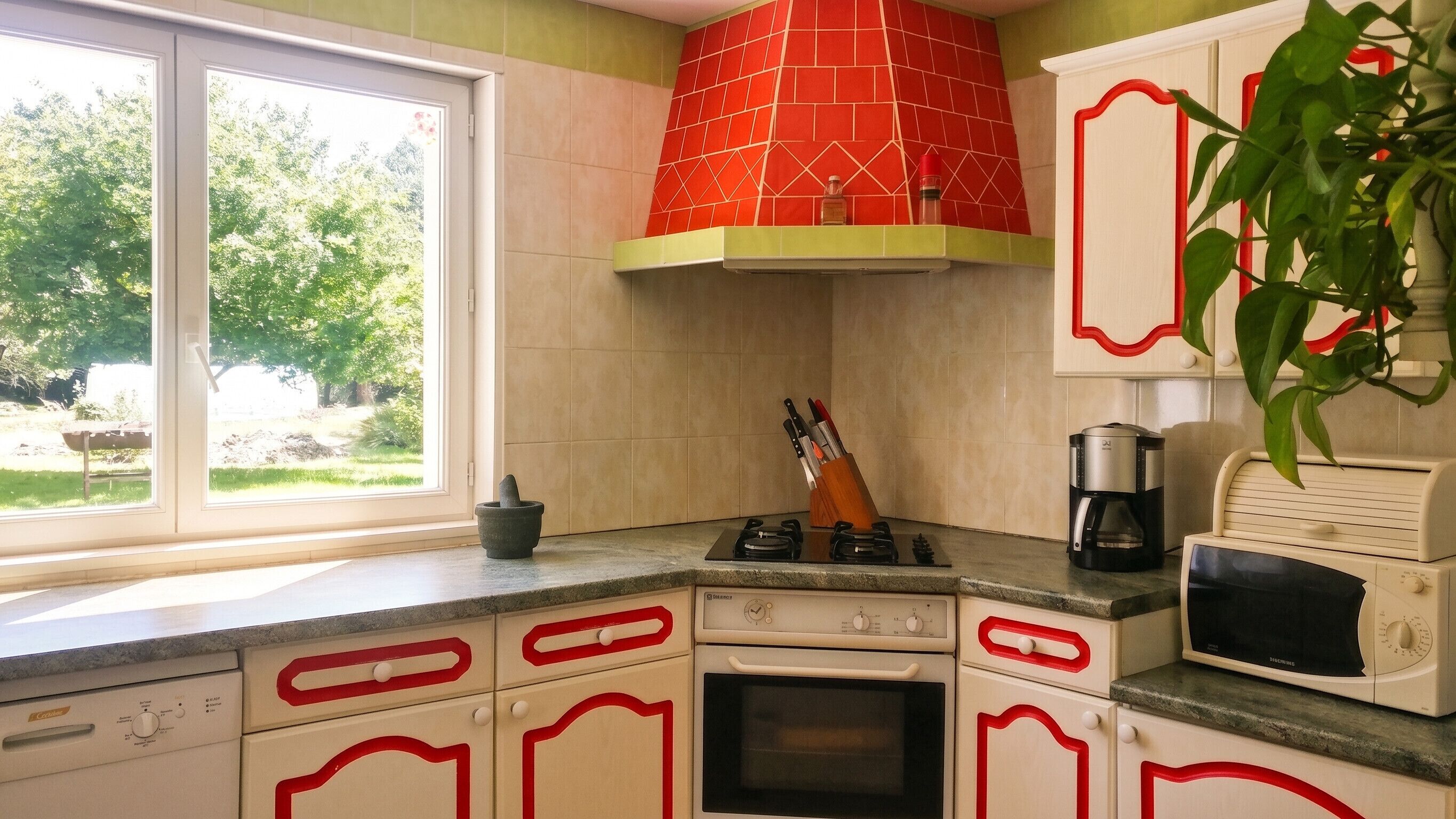 Et køkken med gasblus, ovn, mikroovn og et backsplash med røde fliser.