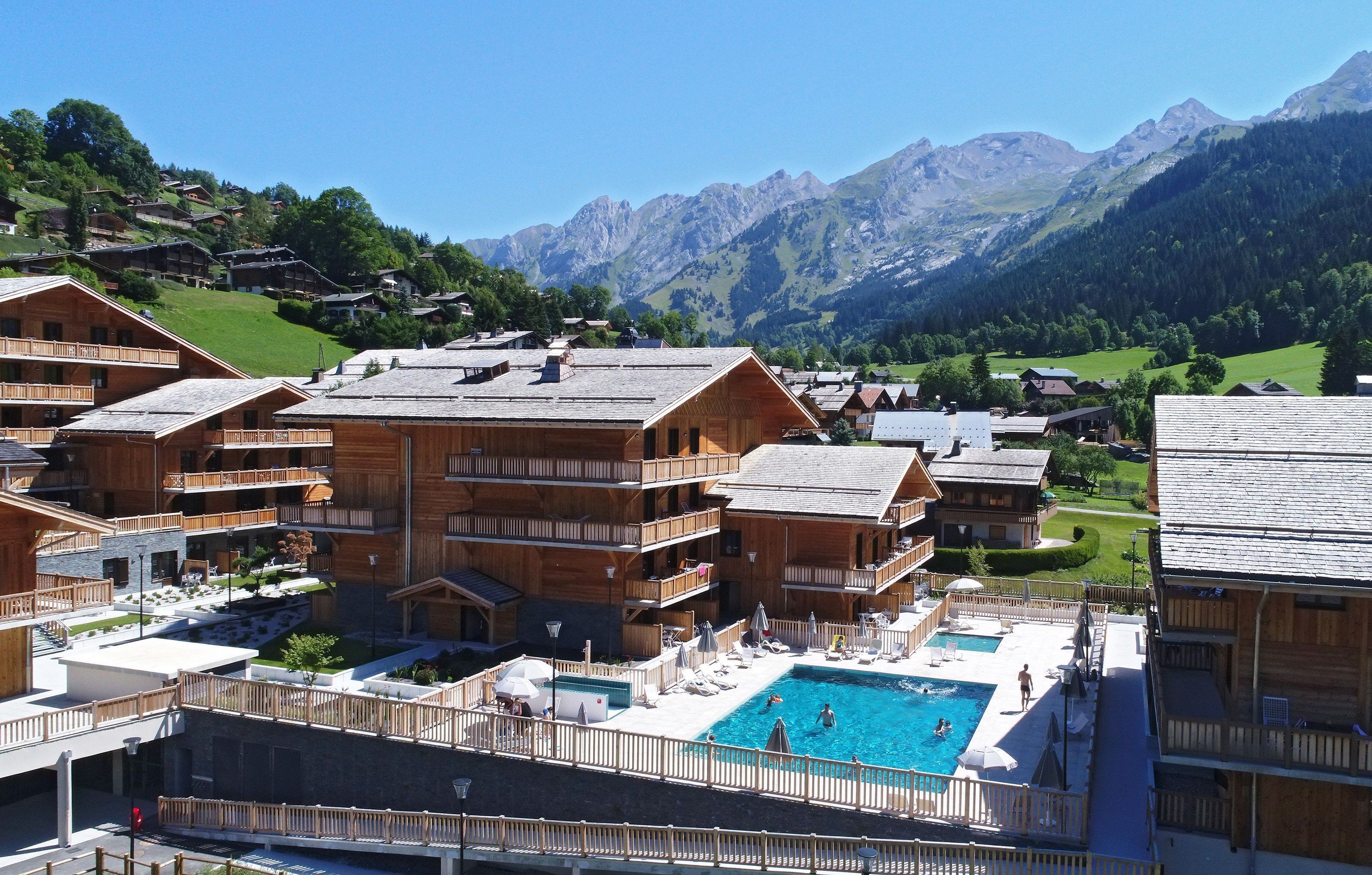A wooden chalet-style hotel with a pool and mountain views.