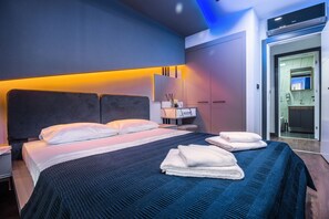 Une chambre d’hôtel moderne, dotée d’un grand lit, d’une table de chevet, d’un bureau et d’une salle de bain visible à travers une porte ouverte.