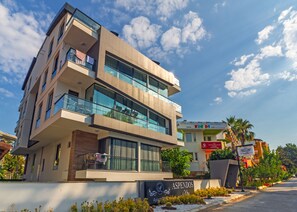 Un immeuble à plusieurs étages doté de balcons, de grandes fenêtres et d’une enseigne indiquant « Hôtel Aspendos ».