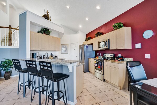 A modern kitchen with a central island, bar stools, and a dining area with a table and chairs.