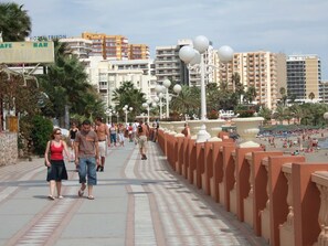 Eine Promenade mit einer Restaurant-Bar, Palmen und einem Strand im Hintergrund.