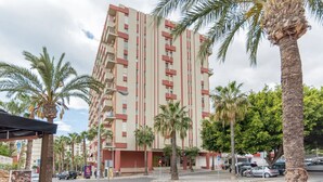 A multi-story hotel with balconies, palm trees, and a street view. - Cozy apartment with pool and sea views (Benalmádena)
