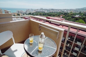 A balcony with a table and two chairs, overlooking a cityscape and the sea.