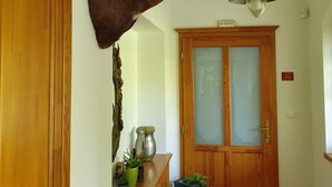 A hallway with a mounted deer head on the wall, a wooden door, a potted plant, and a hanging light fixture.