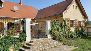 A two-story house with a red-tiled roof, a satellite dish, and a gated entrance.