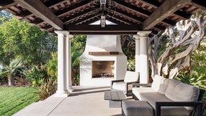 Une terrasse extérieure dotée d’une cheminée en pierre, de colonnes blanches et d’une pergola en bois.