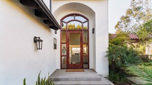 Une entrée de maison avec une porte en bois, un paillasson et un petit jardin avec des plantes.