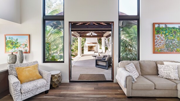 Un salon moderne avec un canapé, un fauteuil et une vue sur une terrasse extérieure, accessible par une porte vitrée, où se trouve une cheminée.