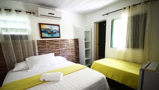 Une chambre d’hôtel avec un lit, une table de chevet, une fenêtre avec des rideaux, un tableau au mur et une porte donnant sur une autre pièce.
