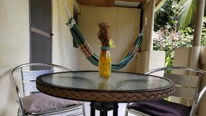 Une table ronde en verre, avec des chaises en métal, un bord de table en fibres tressées et une bouteille décorée de fleurs séchées.