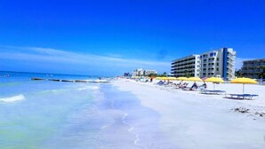 A beach with white sand, clear blue water, and a row of yellow umbrellas. - Now Open! 7-Night Deal – Oceanfront w/ Private Balcony & Stunning Views (Longboat Key)