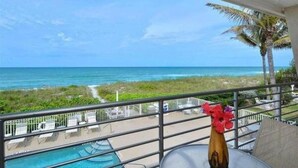 A balcony with a view of the ocean, a pool, and a table with a vase of flowers. - Now Open! 7-Night Deal – Oceanfront w/ Private Balcony & Stunning Views (Longboat Key)