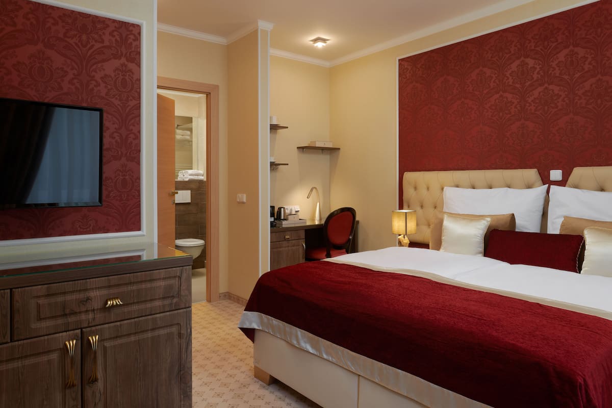 A hotel room with a large bed, a television, a desk, and a bathroom visible through an open door.
