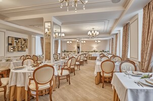 Un comedor amplio con varias mesas y sillas, candelabros y un muro espejado.