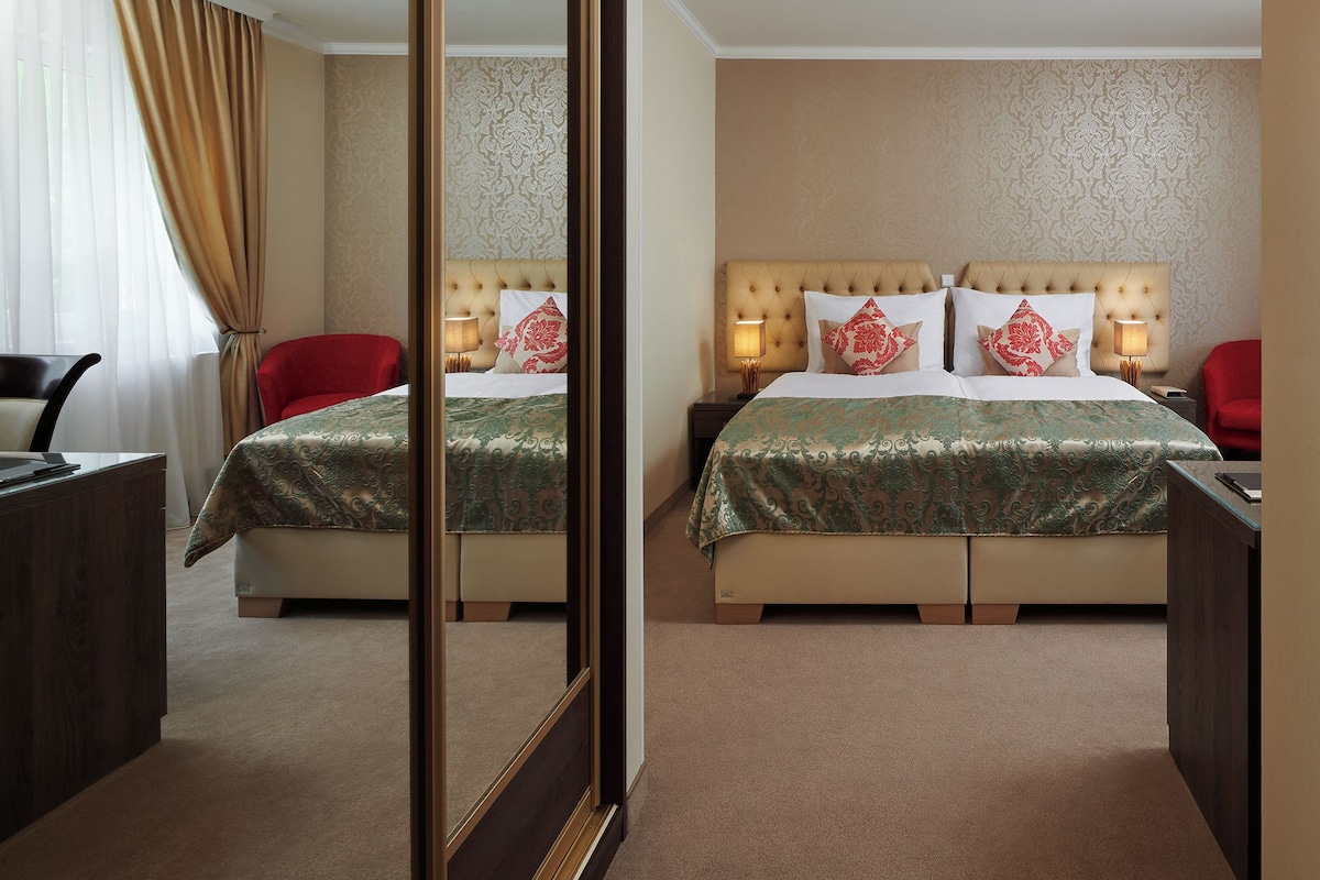 Habitación de hotel con una cama grande, dos mesitas de noche, una silla roja, un escritorio y un espejo.