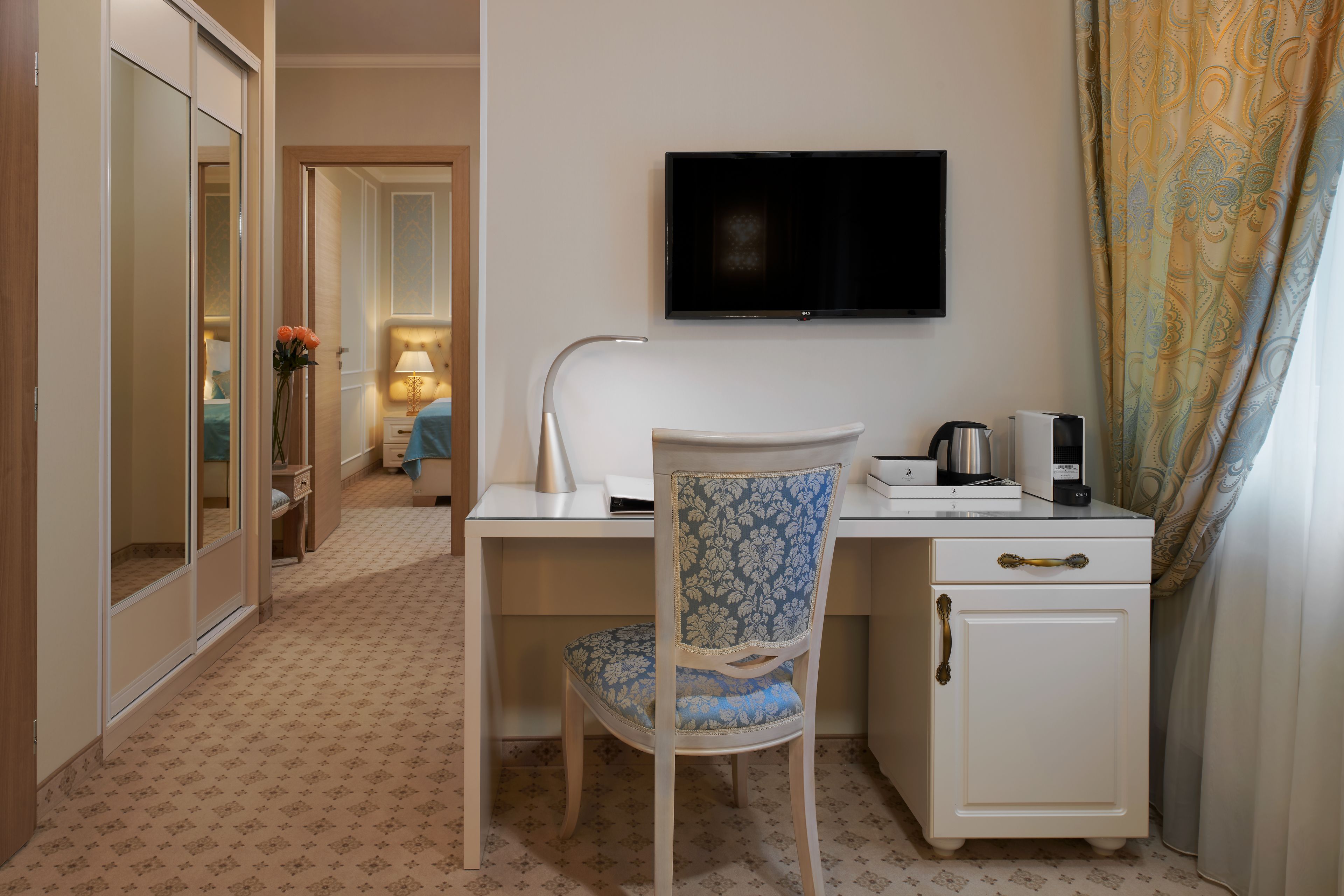 A hotel room with a desk, a chair, a television, a coffee maker, and a wardrobe.