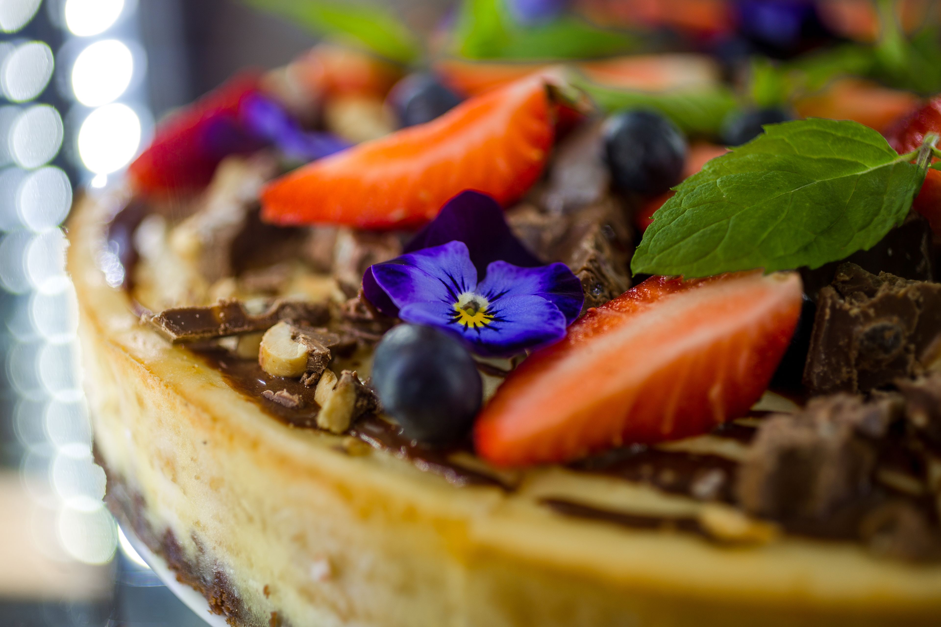 Un gâteau au fromage garni de fraises, de myrtilles, de chocolat et de feuilles de menthe.