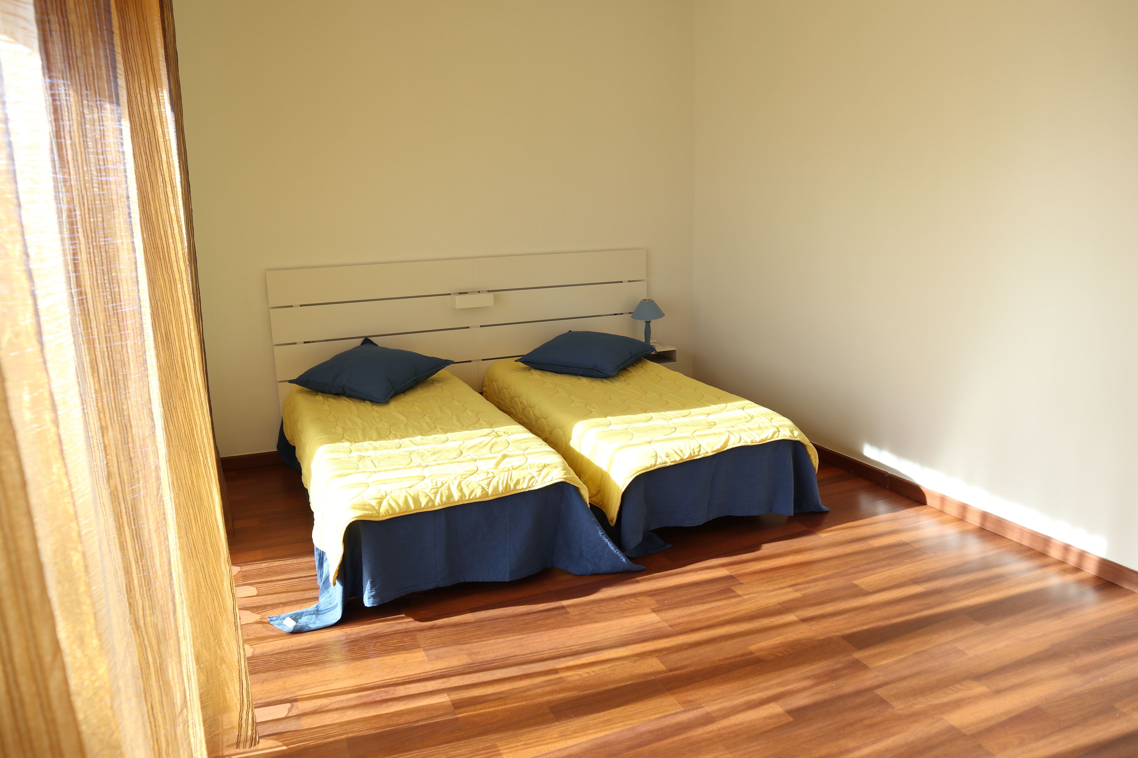 Een kamer met twee bedden, elk met een blauw hoofdeinde en gele beddengoed.