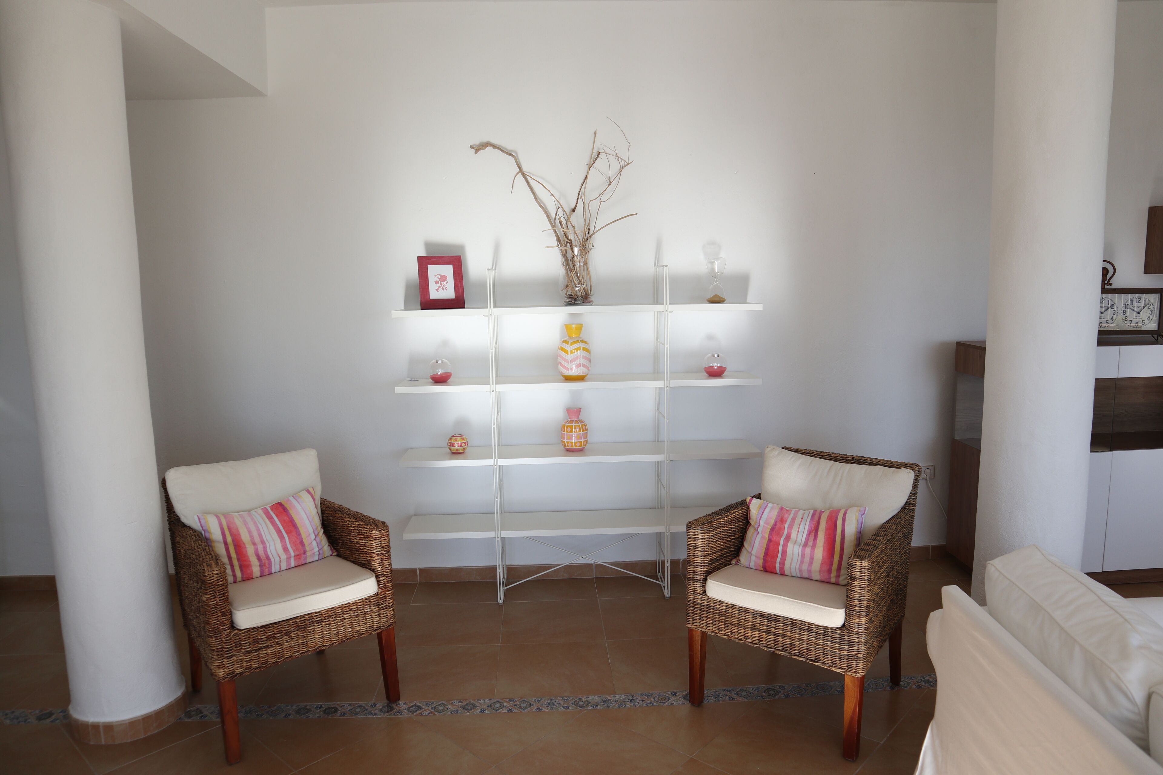 A living area with two wicker chairs, a white sofa, and a white shelving unit with decorative items.