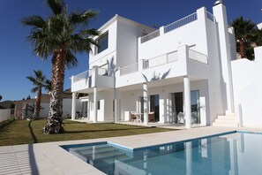 Ein modernes, zweistöckiges Haus mit Swimmingpool, Palmen und blauem Himmel.