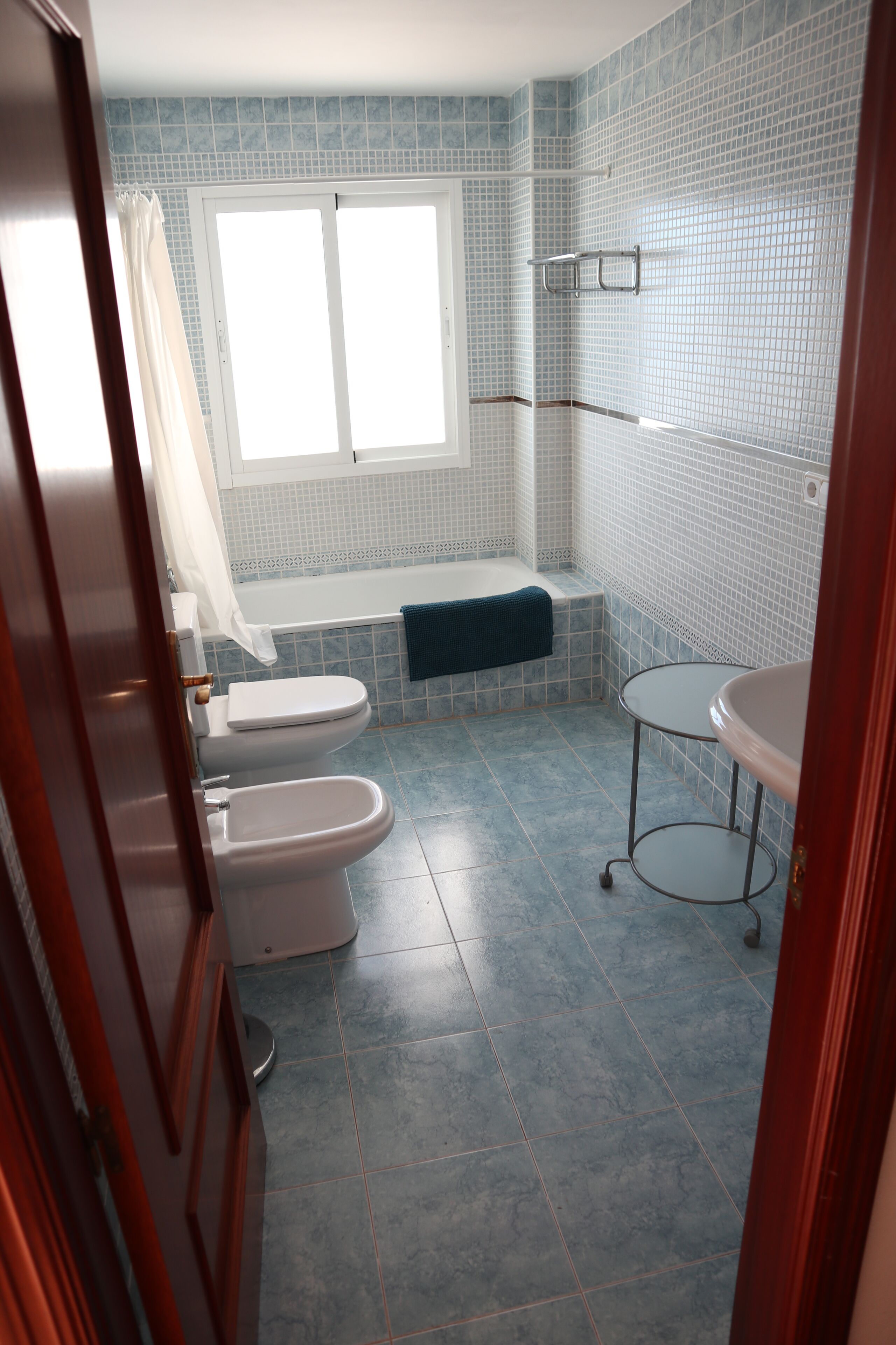 A bathroom with a bathtub, two toilets, a sink, and a window.