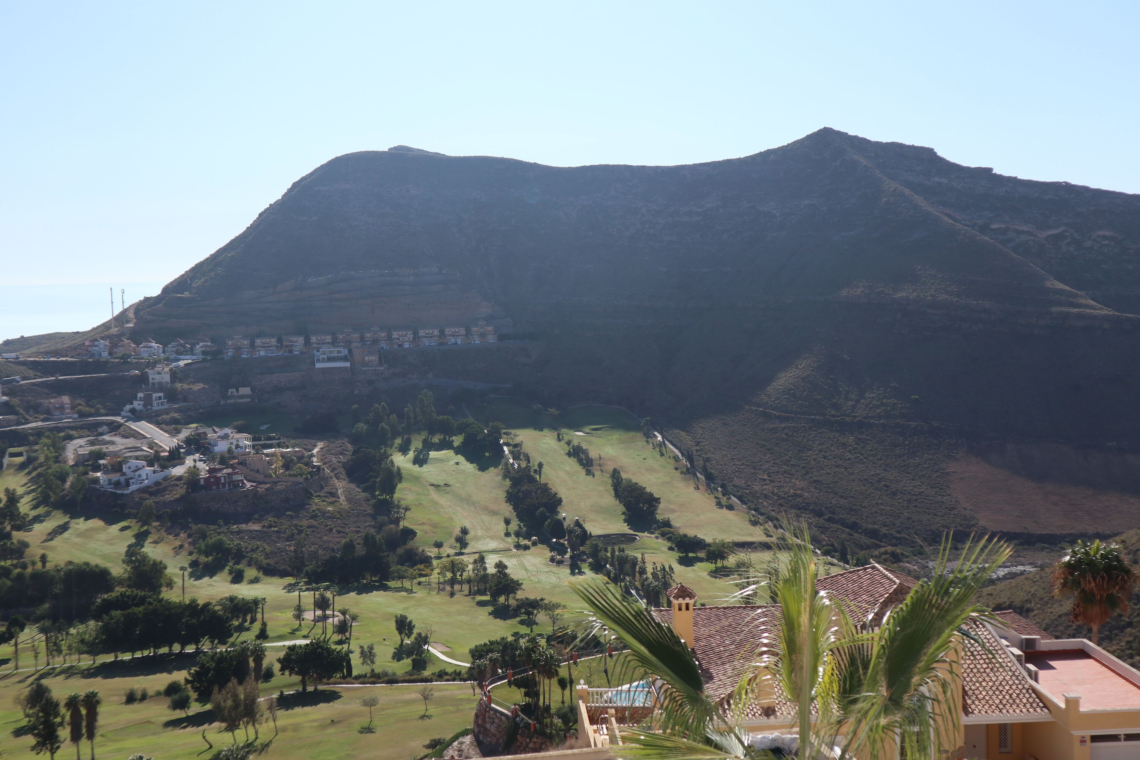 A mountainous landscape with a residential area in the foreground, featuring houses with tiled roofs and a prominent building with a tower.