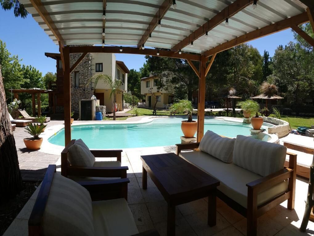 Un espacio de estar al aire libre cubierto con piscina, muebles de madera y un edificio de piedra al fondo.
