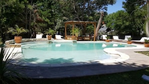Une piscine agrémentée d’un gazebo en bois et de chaises longues.