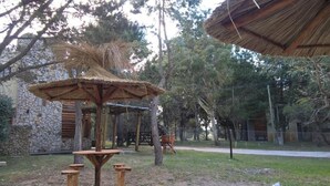 Un espace extérieur rustique agrémenté d’un kiosque en bois, de tables de pique-nique et, au fond, d’un bâtiment en pierre.