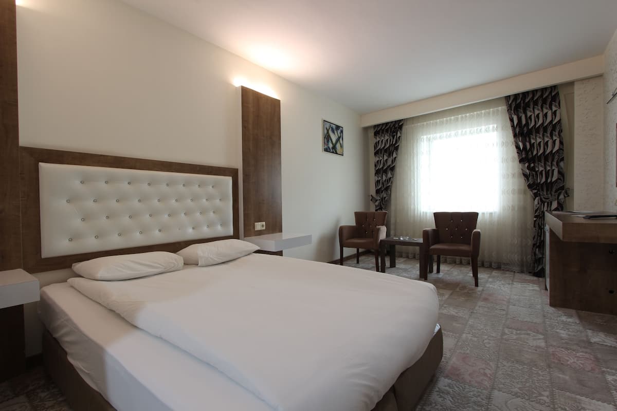 Ein Hotelzimmer mit einem großen Bett, einem hölzernen Kopfteil, einem Schreibtisch, zwei Stühlen und einem Vorhangfenster.