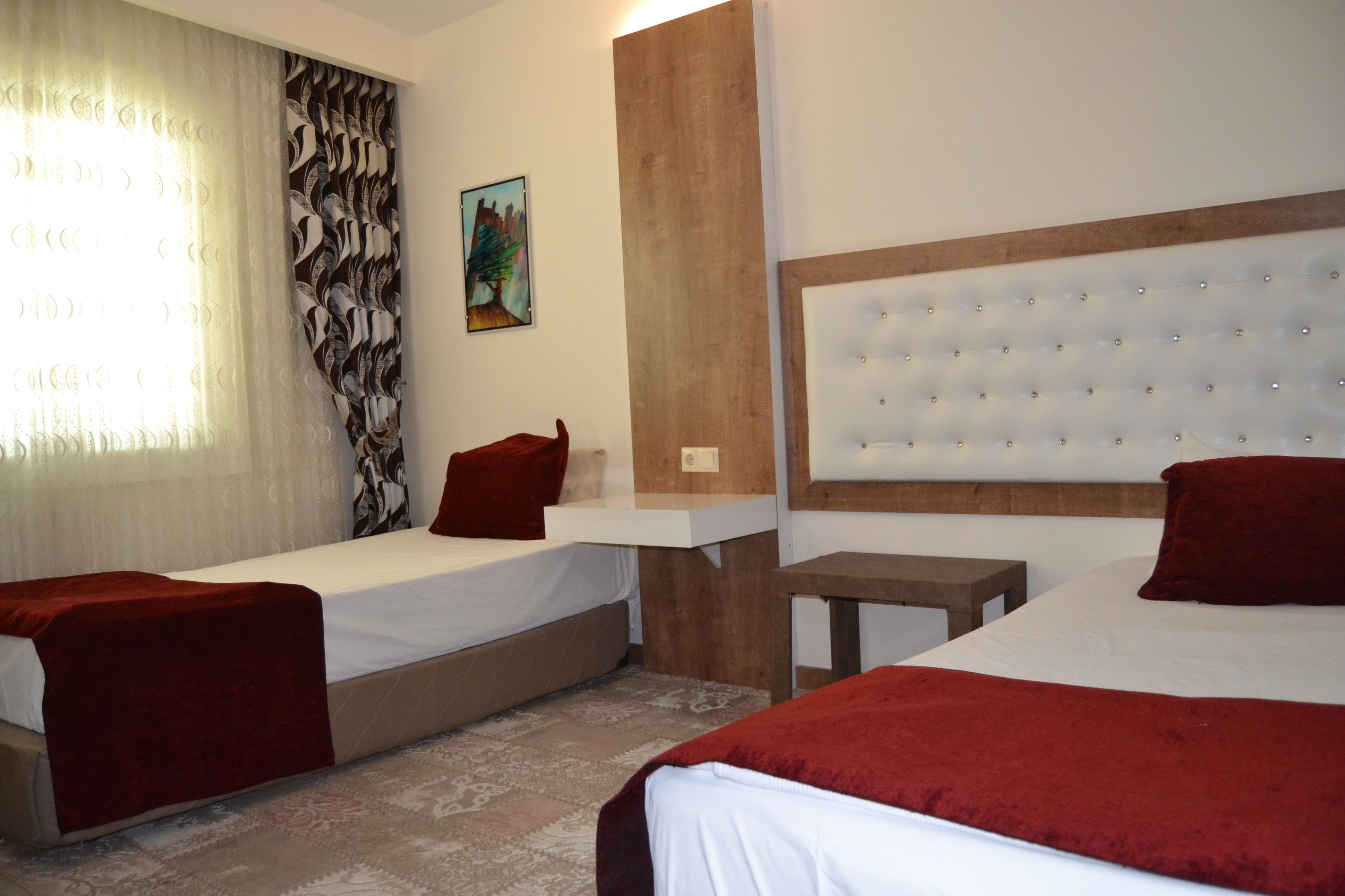 A hotel room with two beds, a wooden headboard, a small table, and a painting on the wall.
