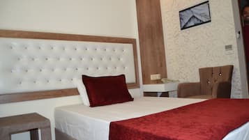 A hotel room with a tufted headboard, a red throw blanket, a wooden nightstand, and a desk with a chair.